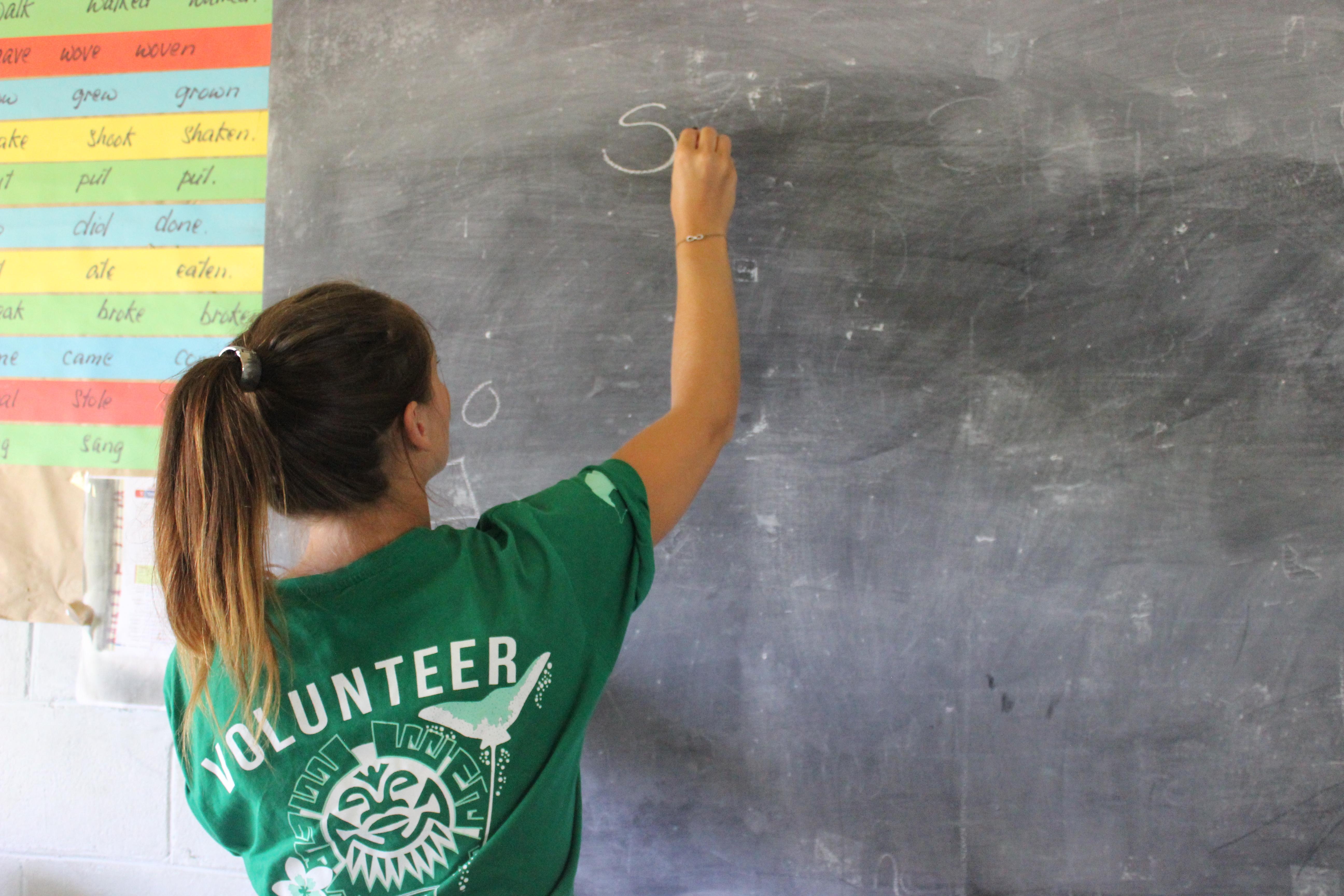 A Projects Abroad volunteer writes on a classroom board during her teaching work experience in Samoa. A volunteer teaching in Samoa writes on a classroom board.